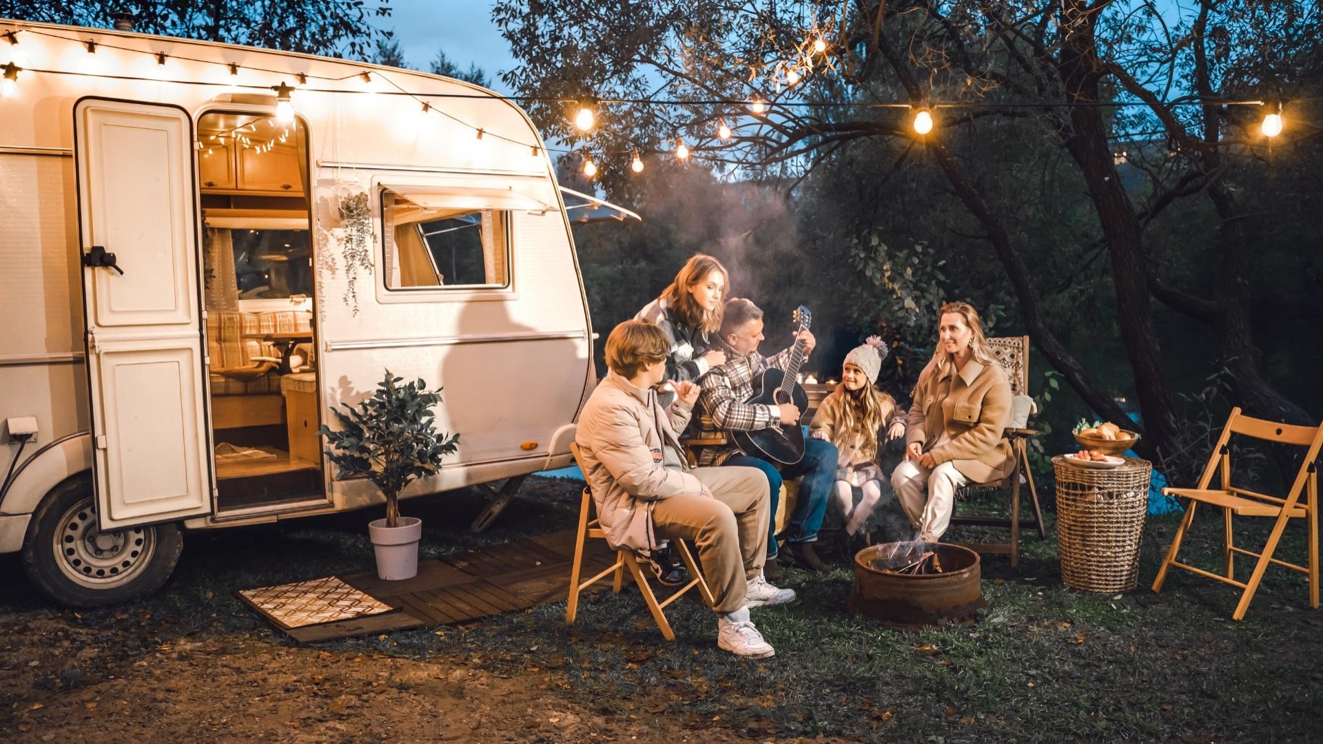 Groupe d'amis se détend près d'une caravane avec une guitare.