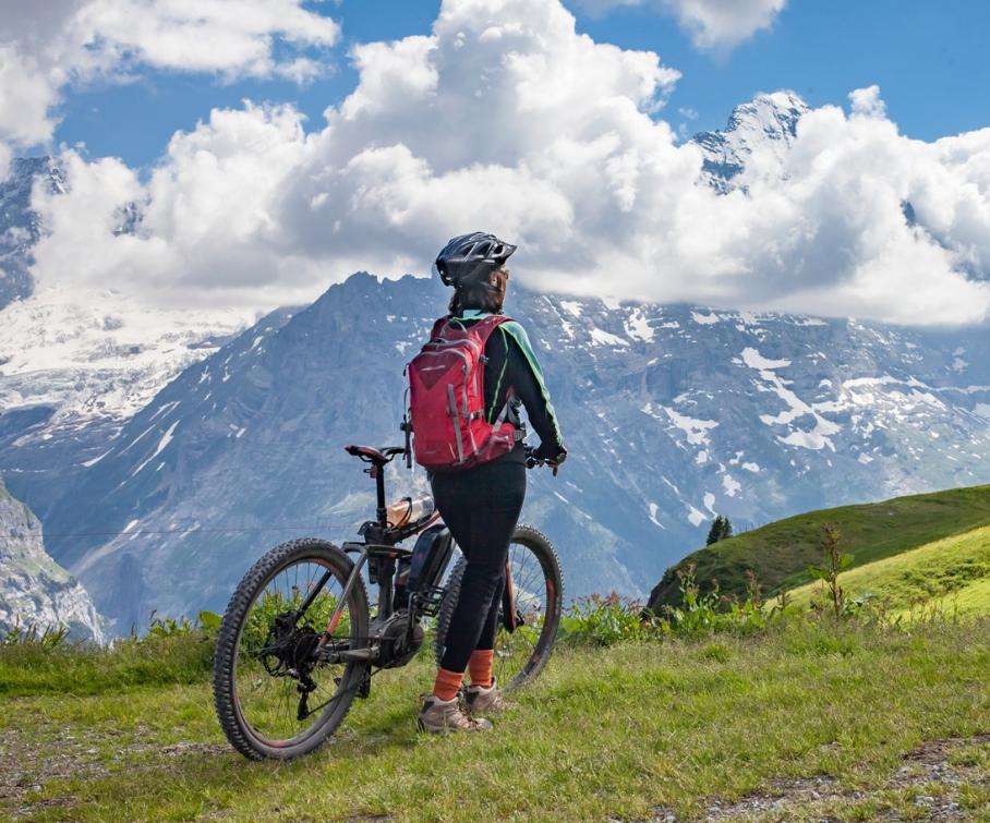 Ciclista ammira montagne innevate sotto un cielo drammatico.