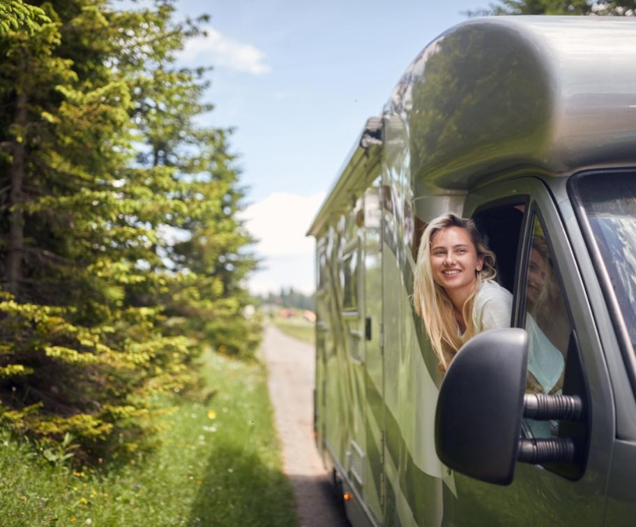 Femme souriante dans un camping-car vert, entourée de nature.